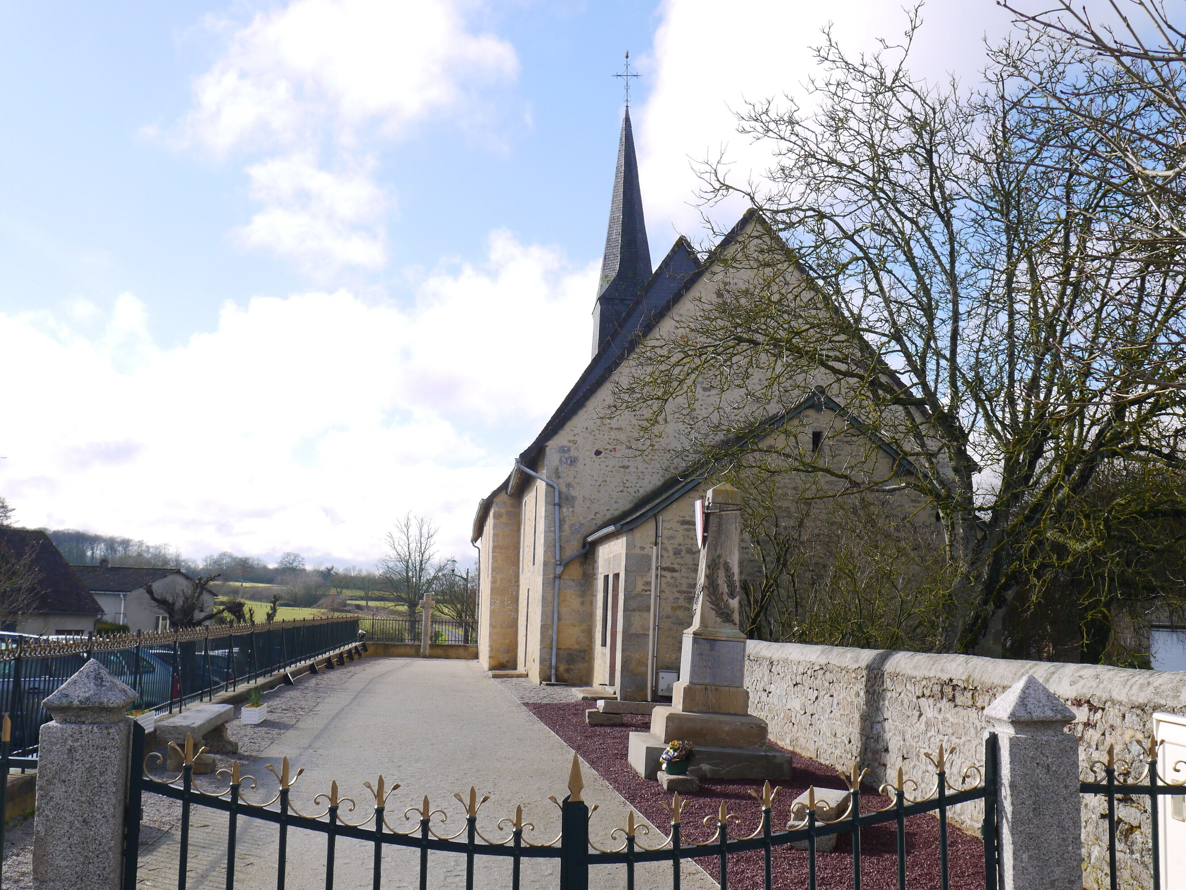 A church with a tall steeple, a stone wall, and a paved pathway leading to the entrance.