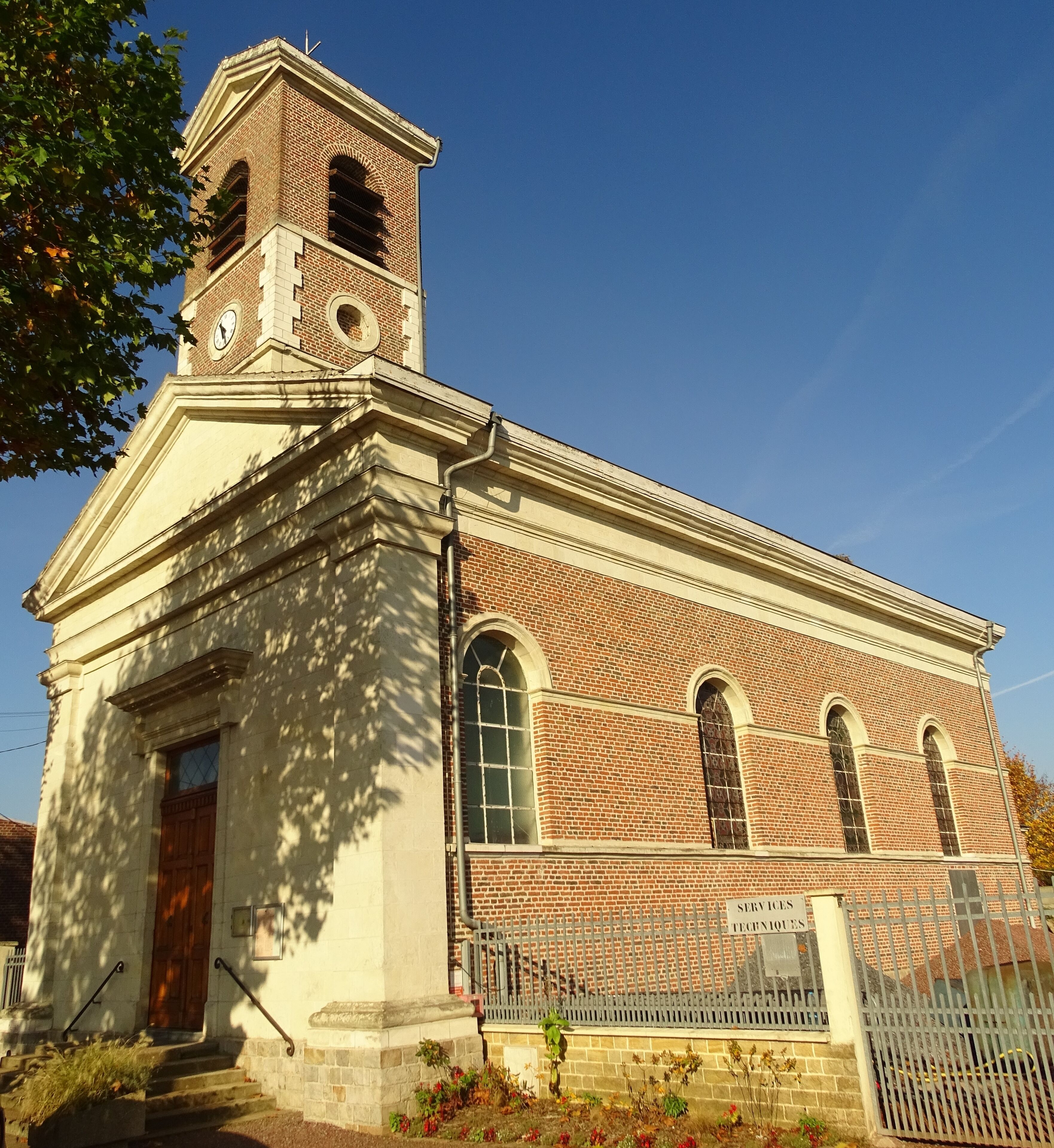 A church with a clock tower, brick facade, and a sign reading "SERVICES TECHNIQUES".