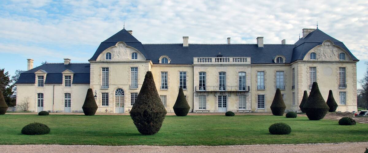 A large stately building with a symmetrical facade, multiple windows, and a well-manicured lawn with topiary sculptures.