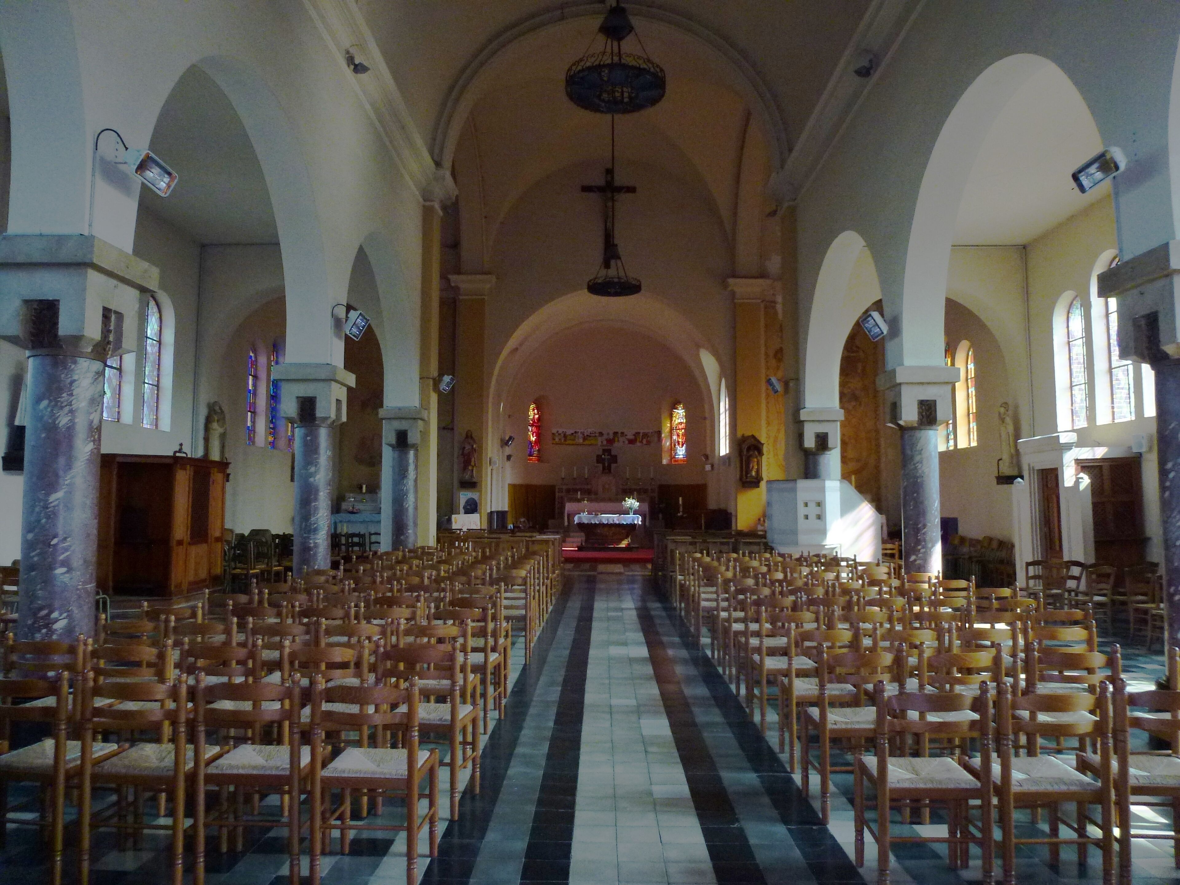 An empty church with rows of wooden chairs, a central aisle, and stained glass windows.