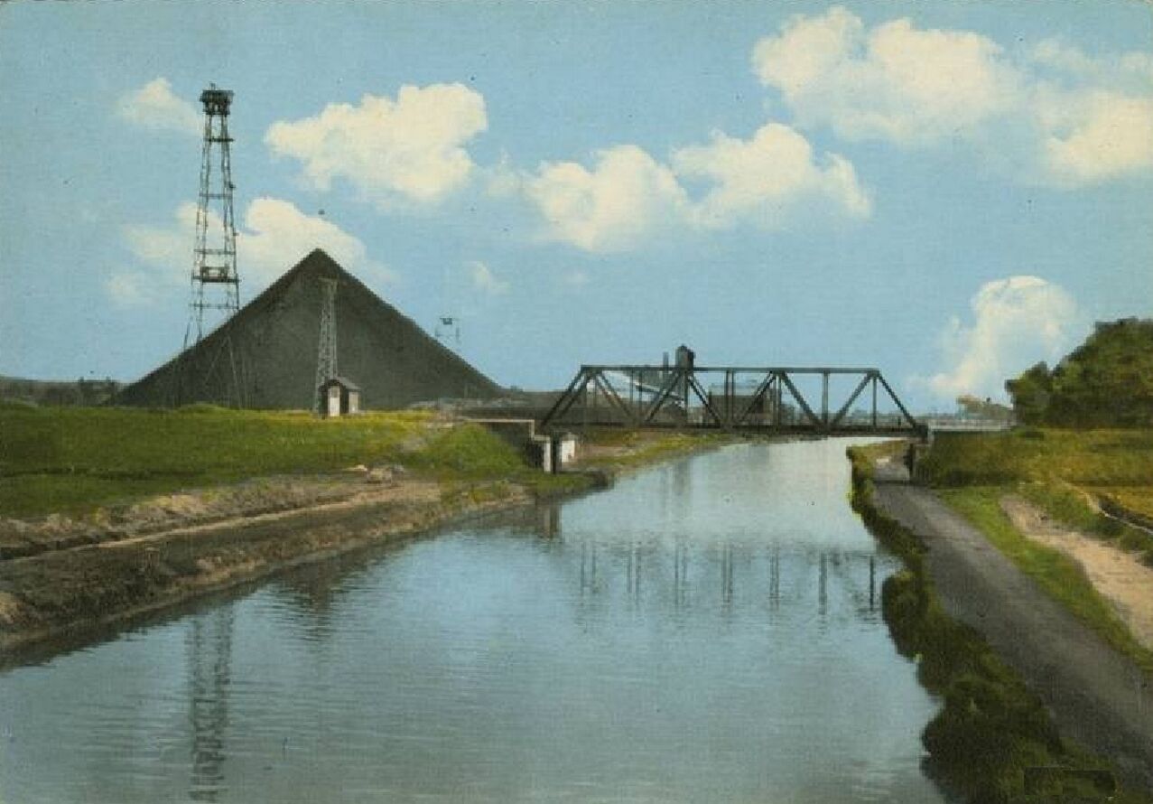 A calm river with a metal bridge and a large pyramid-like structure in the background.