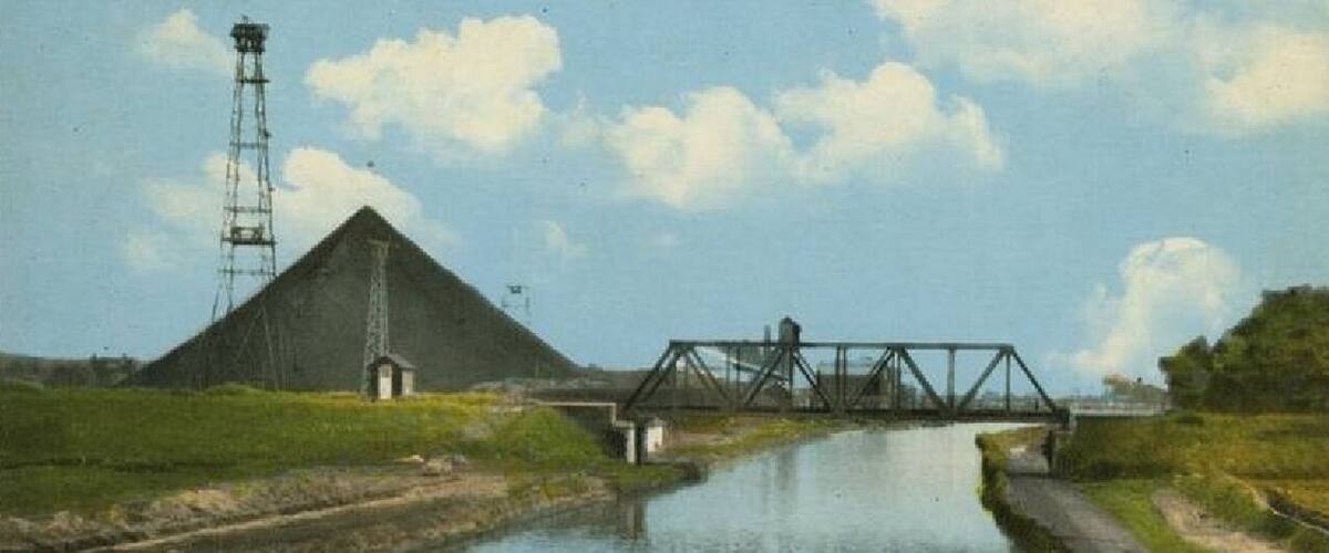 A calm river with a metal bridge and a large pyramid-like structure in the background.