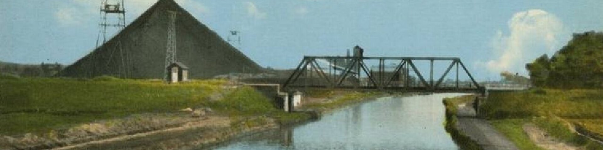 A calm river with a metal bridge and a large pyramid-like structure in the background.