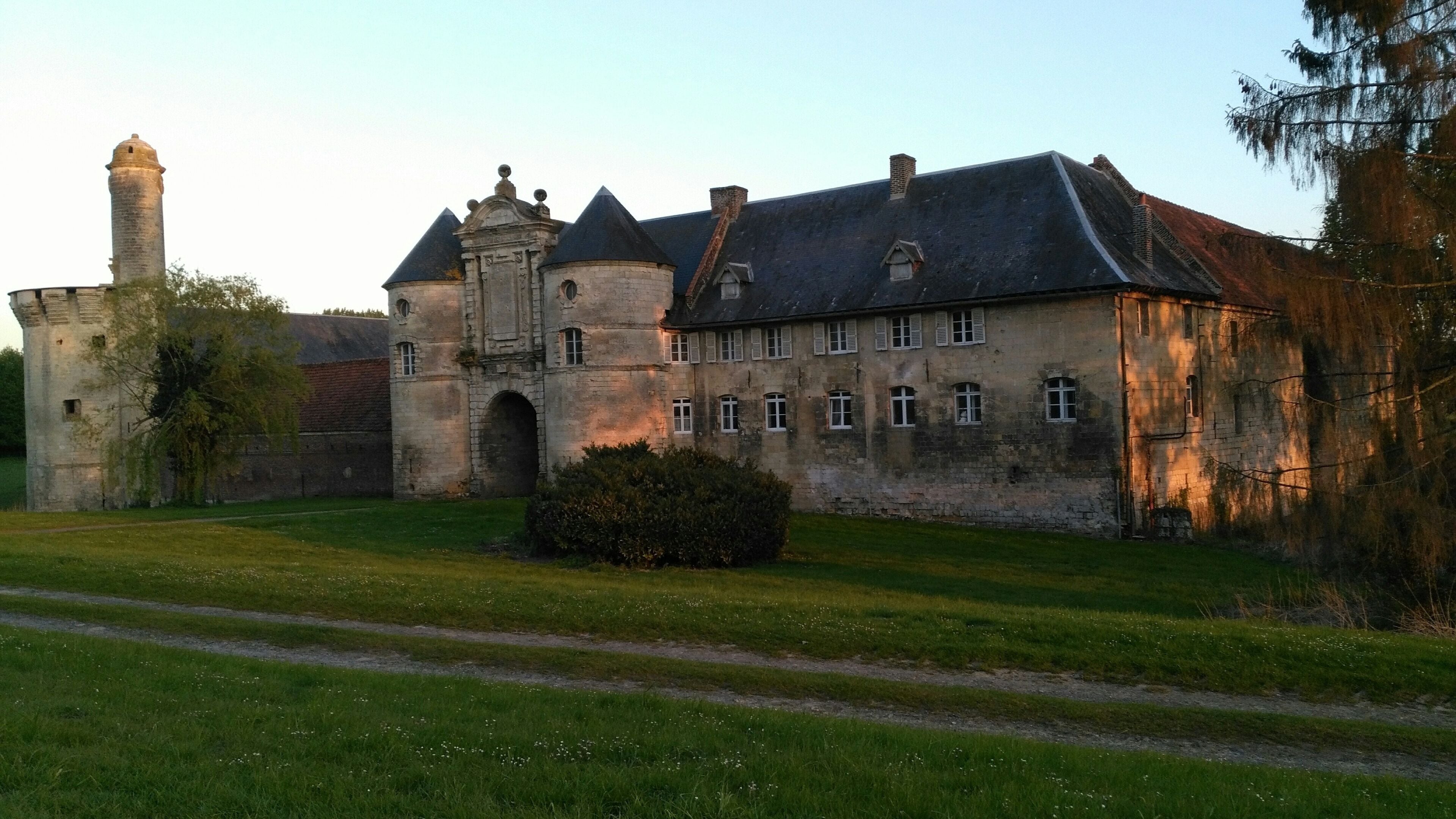 A historic stone building with a tower, surrounded by a well-maintained lawn and a pathway.