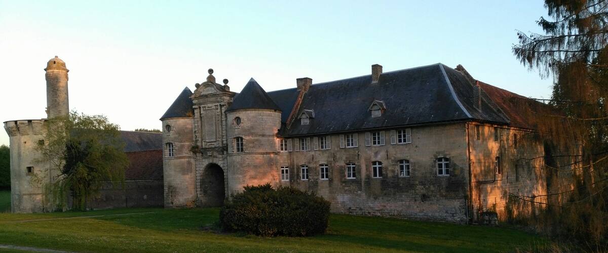 A historic stone building with a tower, surrounded by a well-maintained lawn and a pathway.