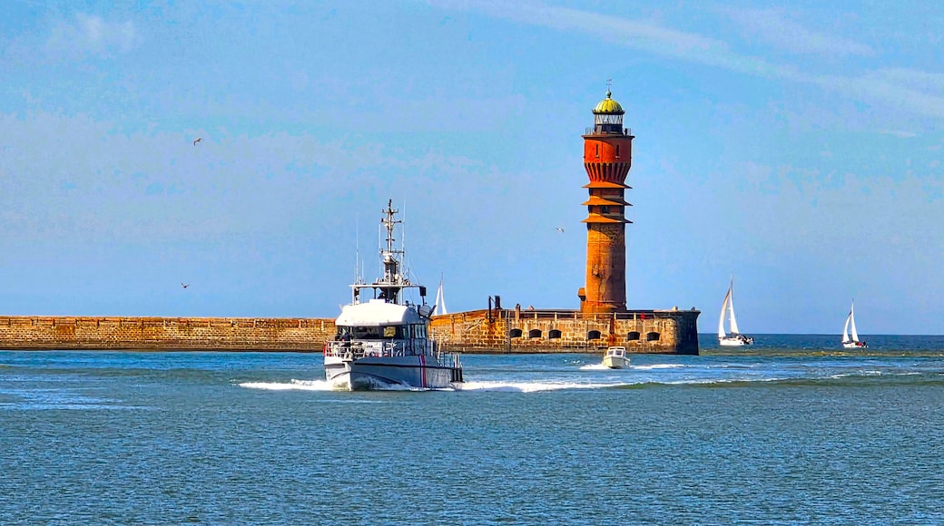 Een vuurtoren, een boot en zeilboten op het water.