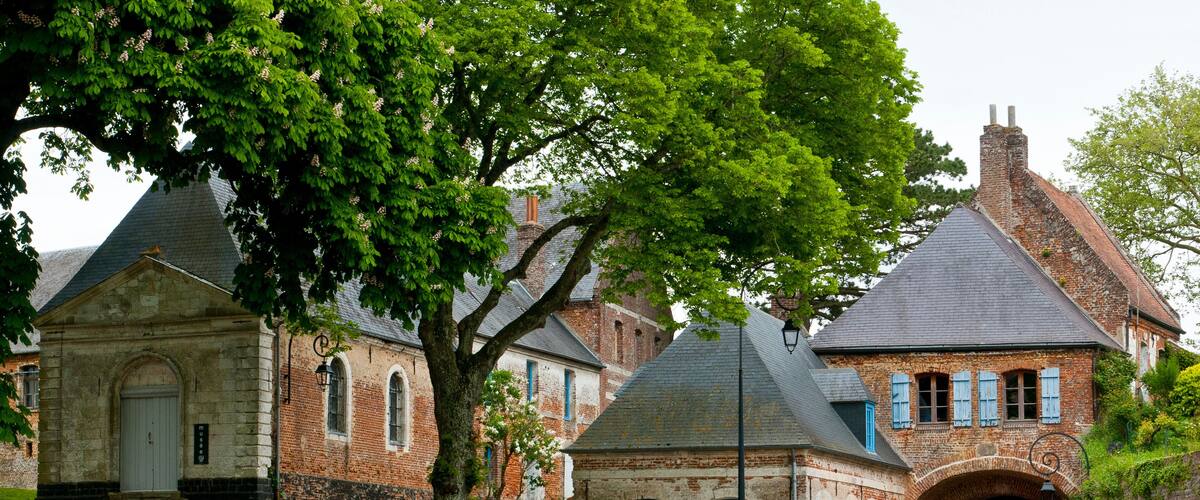 A historic building with a stone facade, a large tree in front, and a brick archway.