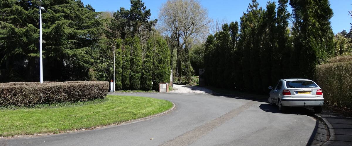 A curved road with a car driving on it, surrounded by trees and a hedge.