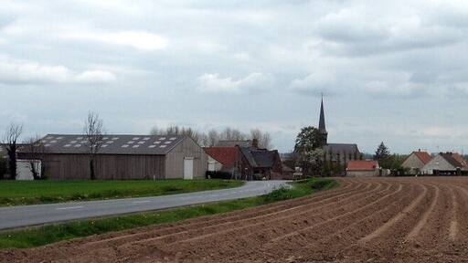 Un paisaje rural con un camino que serpentea por campos, una iglesia con campanario y varias construcciones agrícolas.