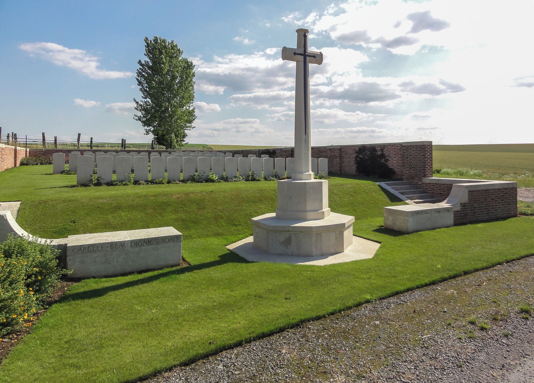 A cemetery with a prominent cross, headstones, and a brick wall.