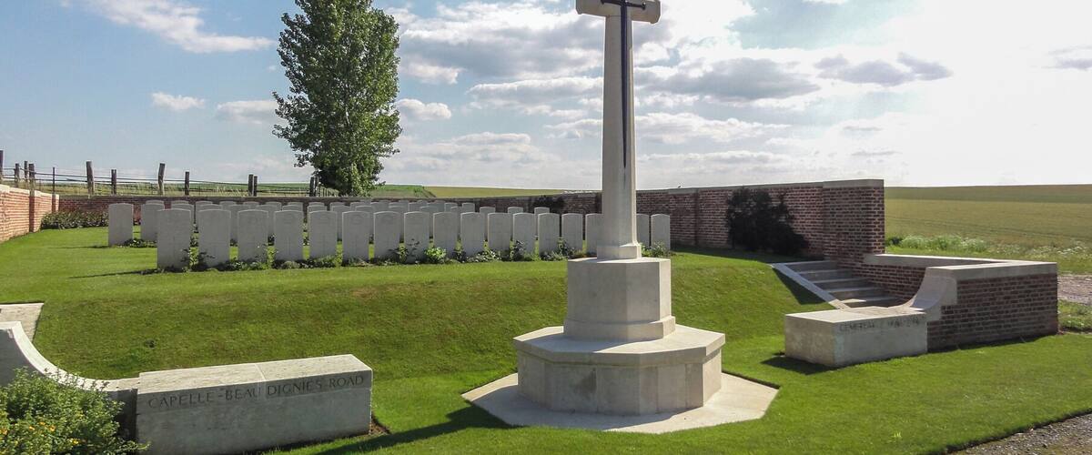 A cemetery with a prominent cross, headstones, and a brick wall.