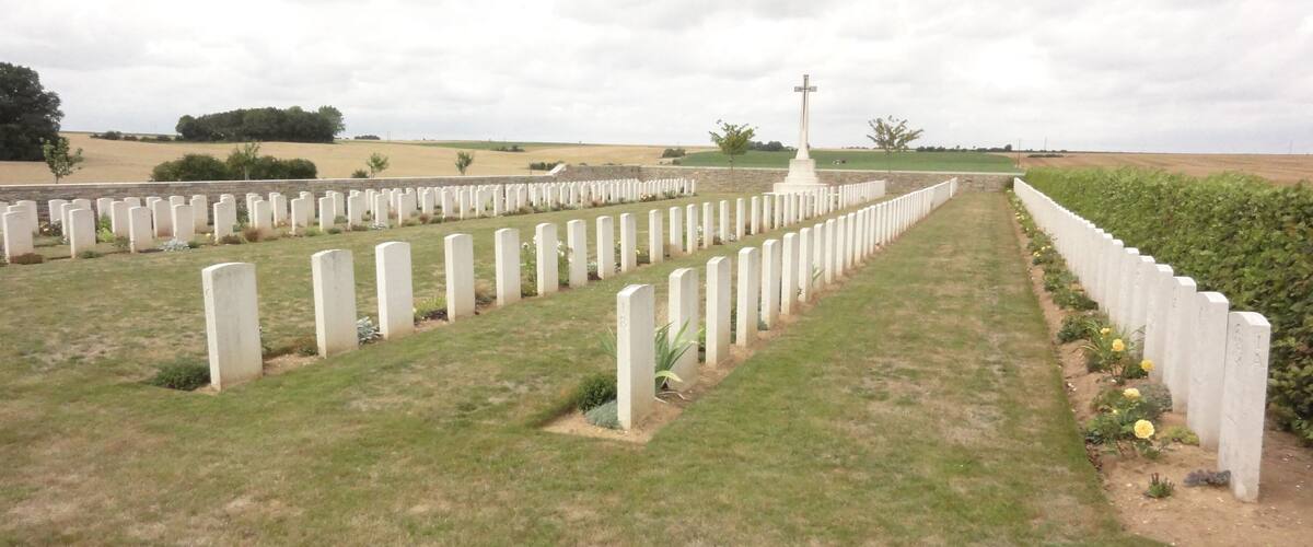 A cemetery with rows of white headstones and a central cross monument.