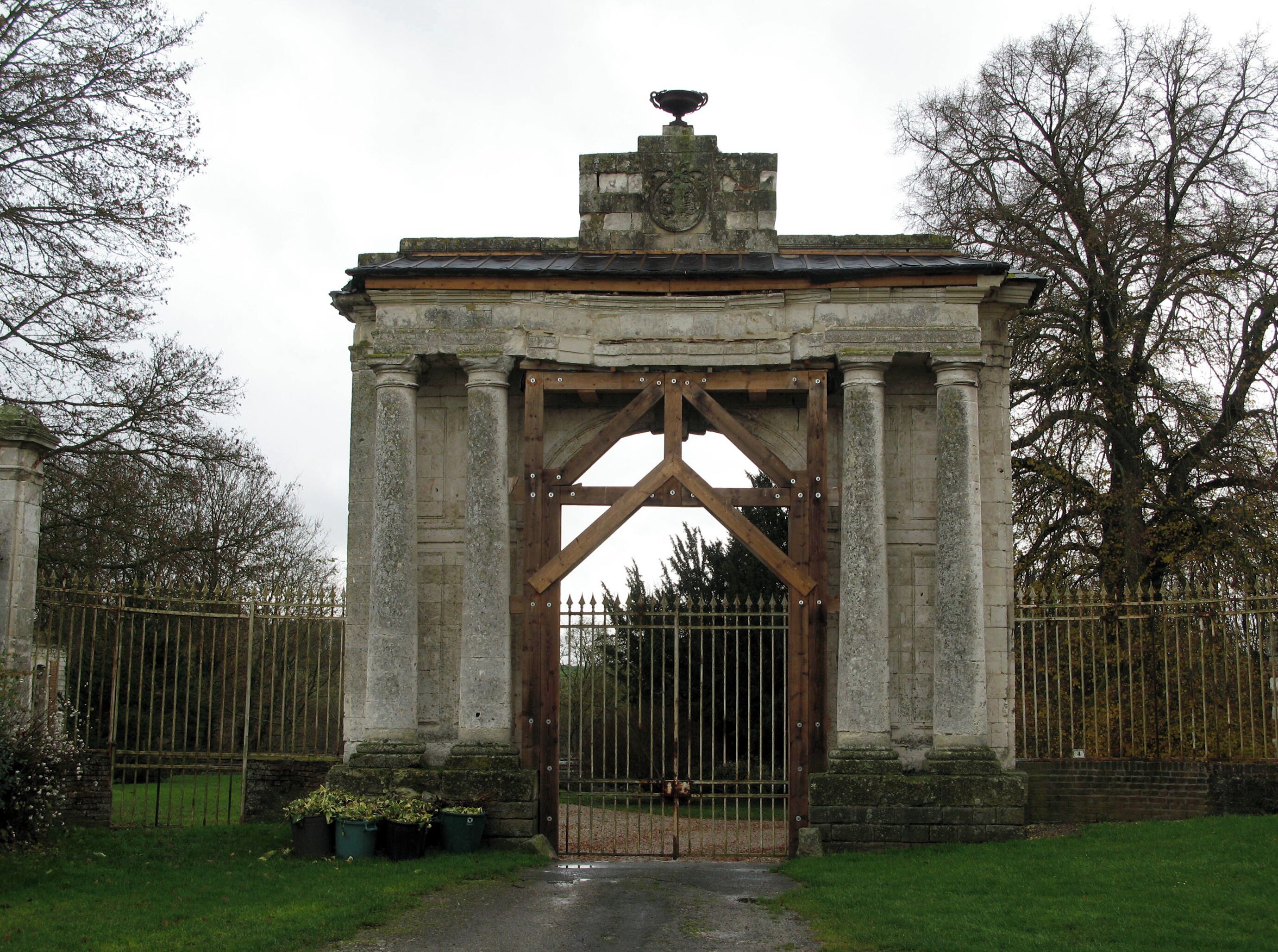 A stone archway with a wooden gate, surrounded by a fence and trees.