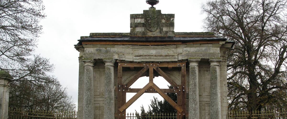 A stone archway with a wooden gate, surrounded by a fence and trees.