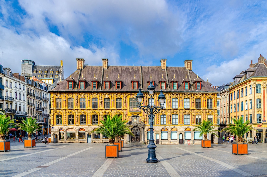 A historic building with ornate yellow facades and red window frames, surrounded by cobblestone streets and palm trees.