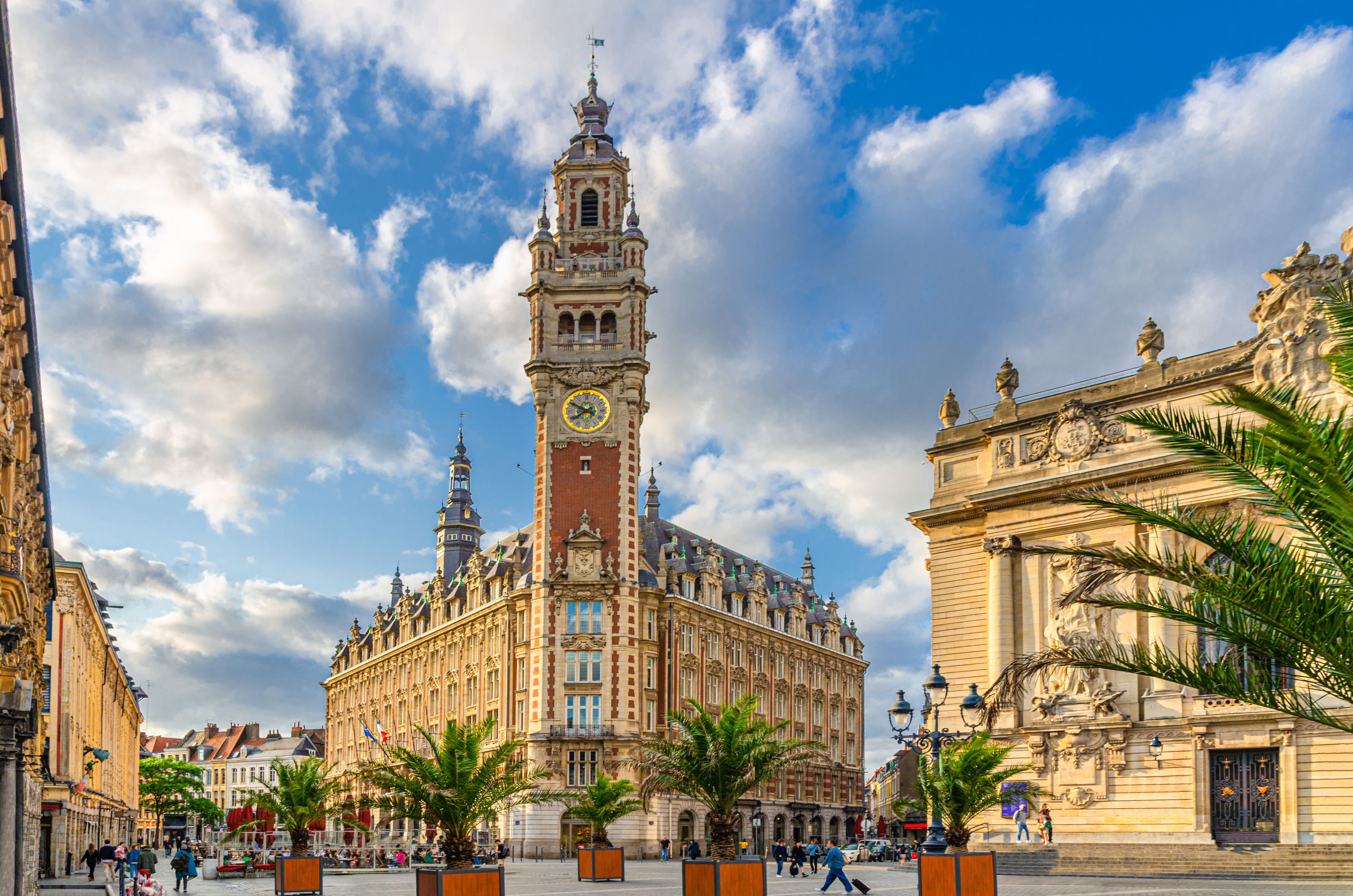 A historic building with a clock tower, palm trees, and a clear blue sky.