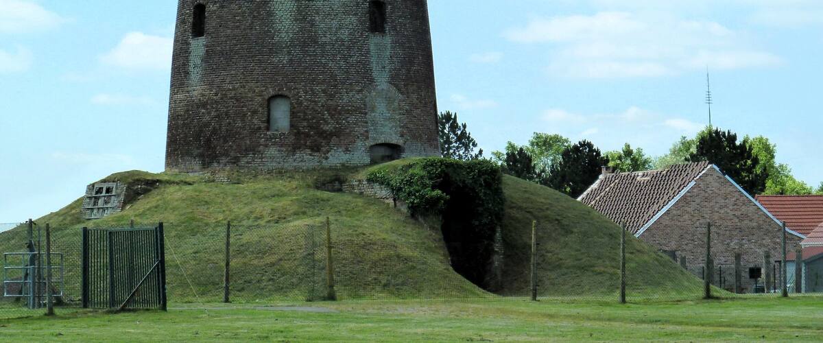 A historic stone tower with a conical roof, surrounded by a grassy area and a small building with a red roof.