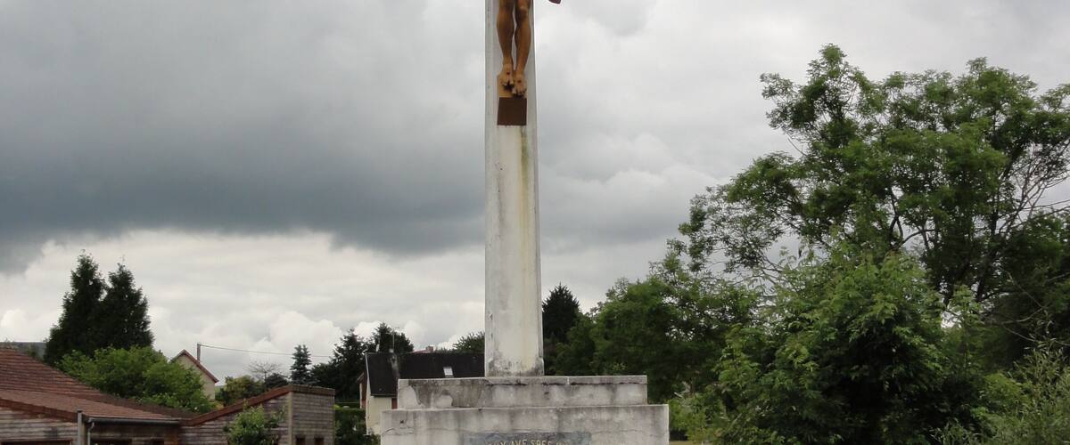 A crucifixion statue with a plaque, surrounded by grass and trees.