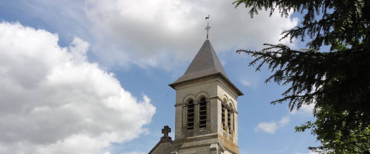 A historic stone church with a tall bell tower and a weather vane, surrounded by a stone wall and trees.