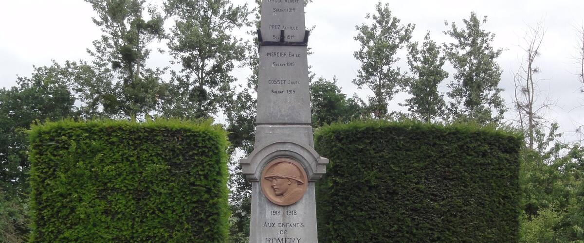 A memorial monument with names and dates, surrounded by hedges and red roses.