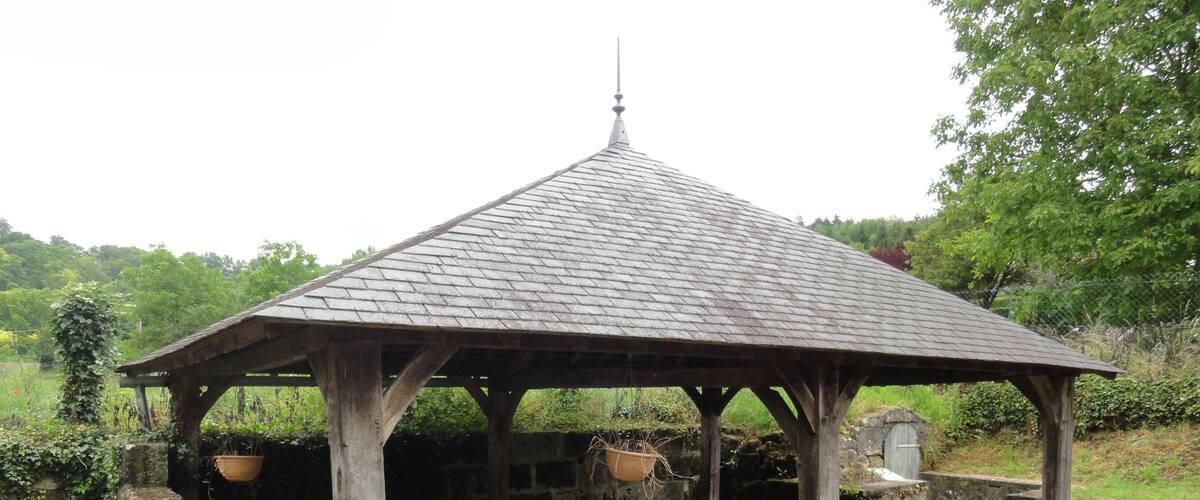 A gazebo with a tiled roof, stone walls, and hanging flower pots.