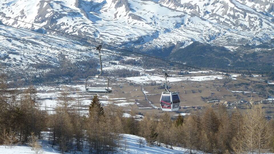 A snow-covered mountain landscape with a ski lift and a cable car system.