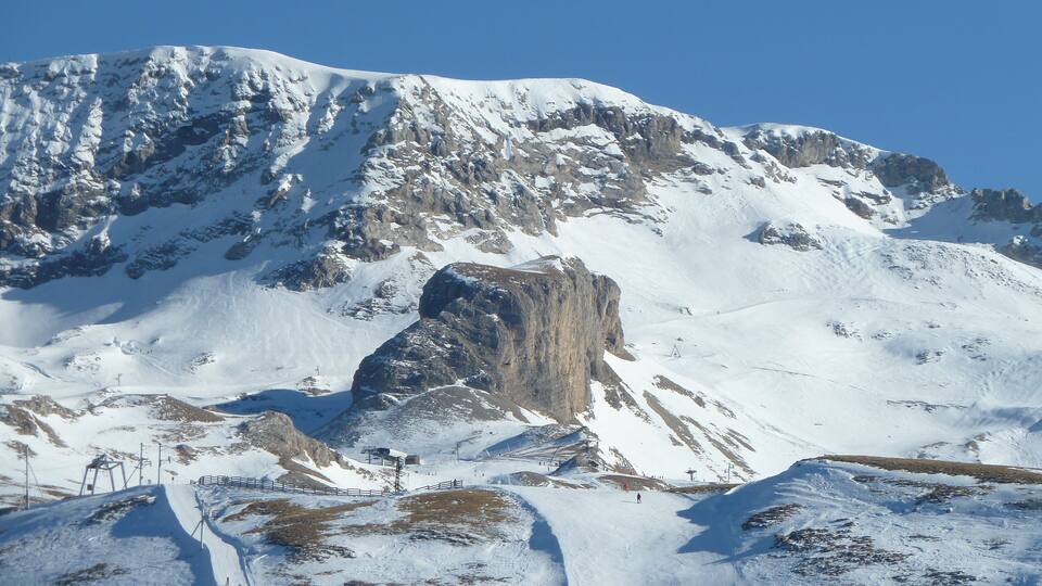 A snow-covered mountain with a rocky outcrop and ski slopes.