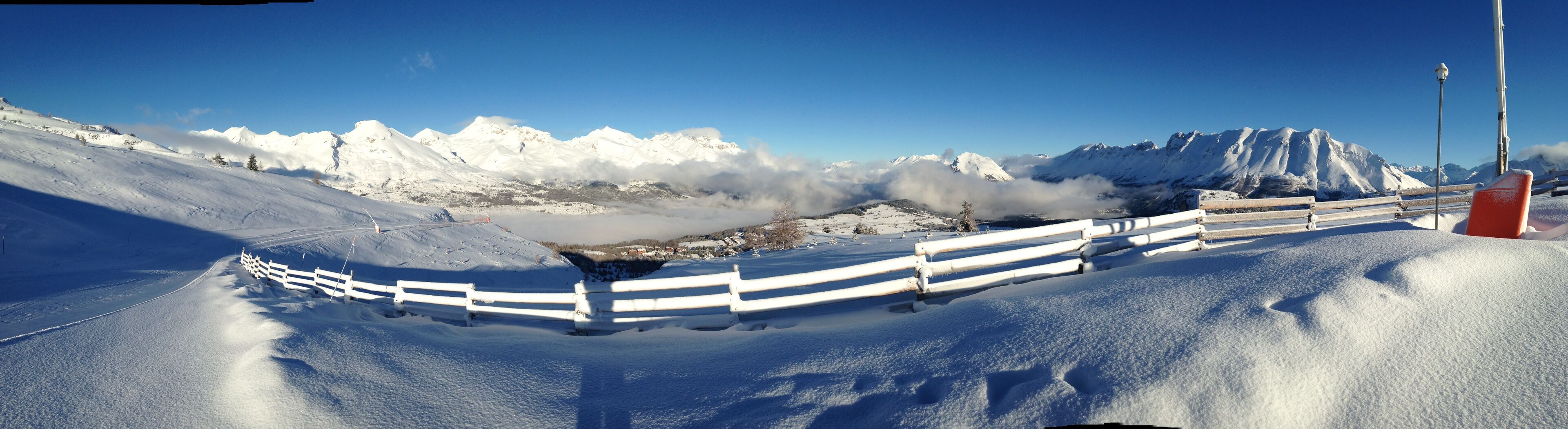 A snow-covered mountain landscape with a white fence and a red sign.