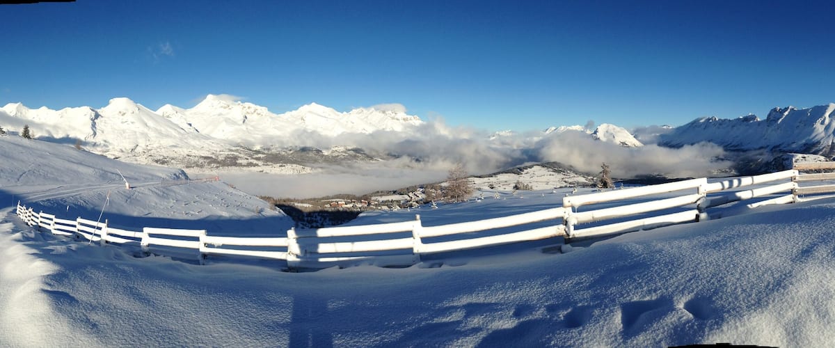 A snow-covered mountain landscape with a white fence and a red sign.