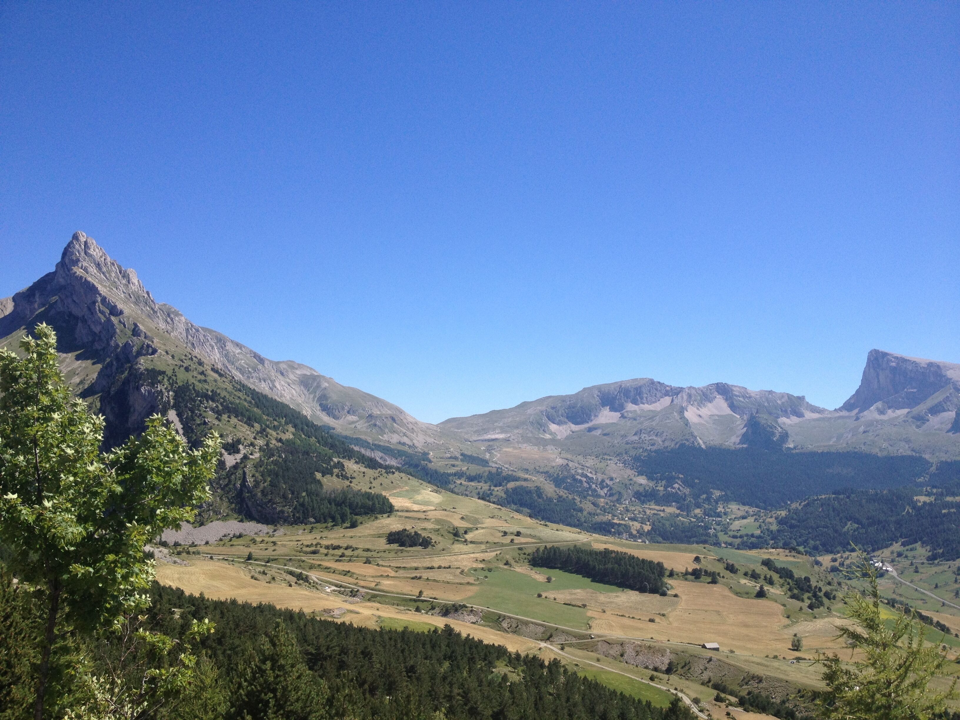 A mountainous landscape with a prominent peak, rolling hills, and a valley with scattered trees and fields.