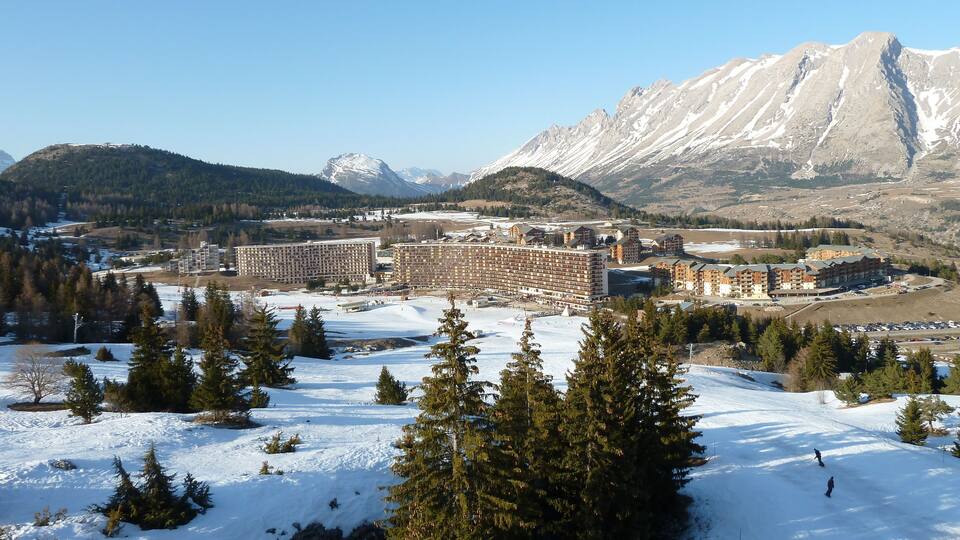 A snow-covered landscape with a large building complex and mountains in the background.
