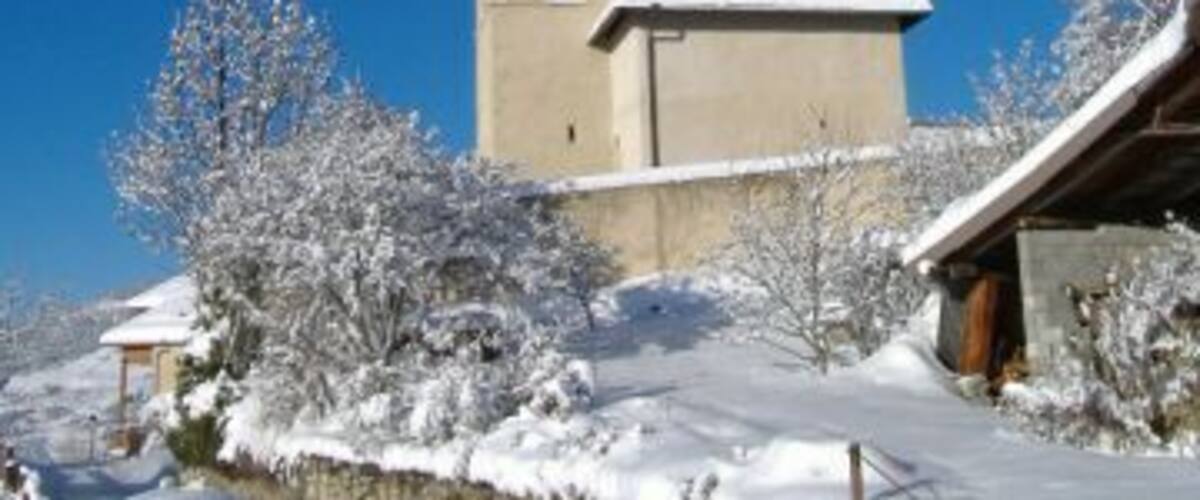 A snow-covered church with a tall bell tower and a stone wall in the foreground.