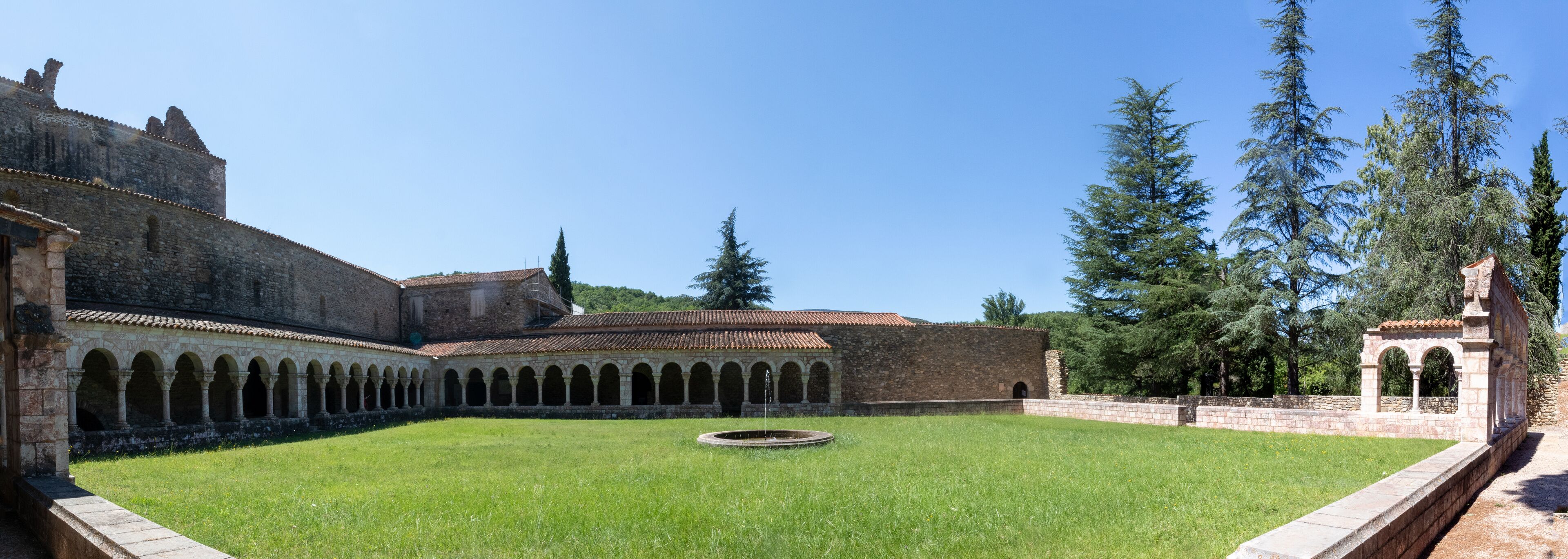 A courtyard with a fountain, surrounded by stone buildings and tall trees.
