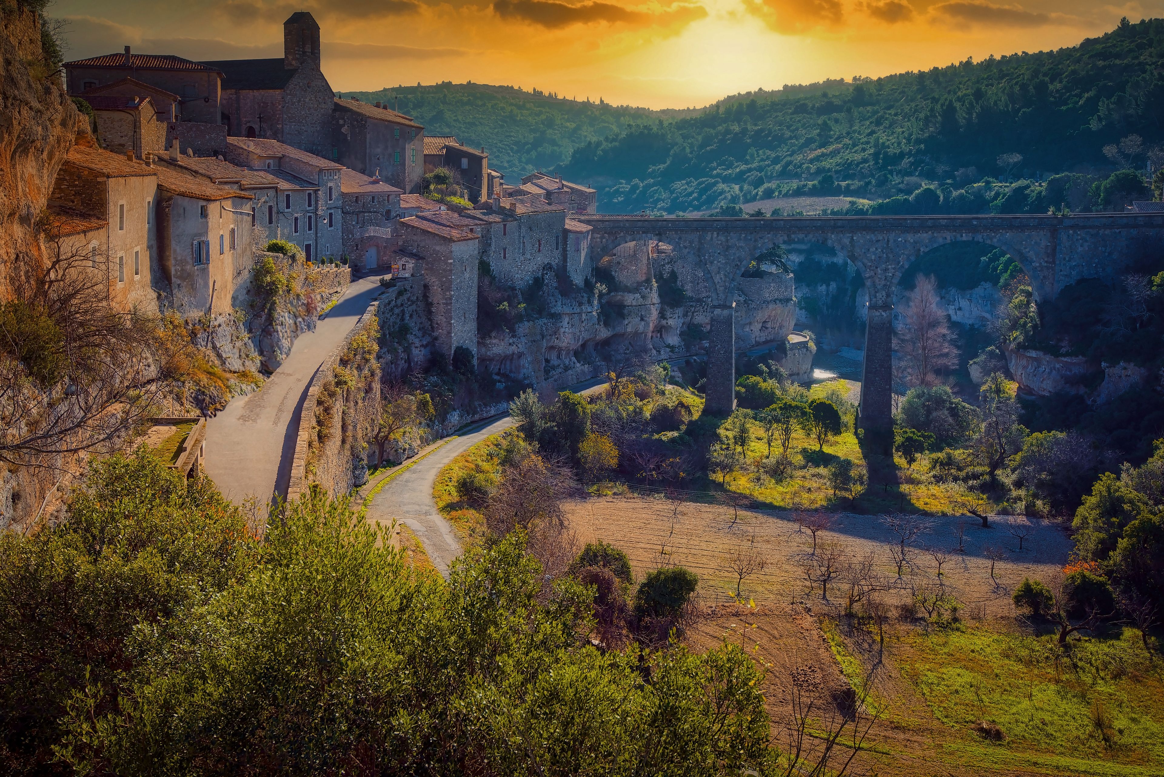 A historic town with stone buildings, a winding road, and a stone bridge over a river.