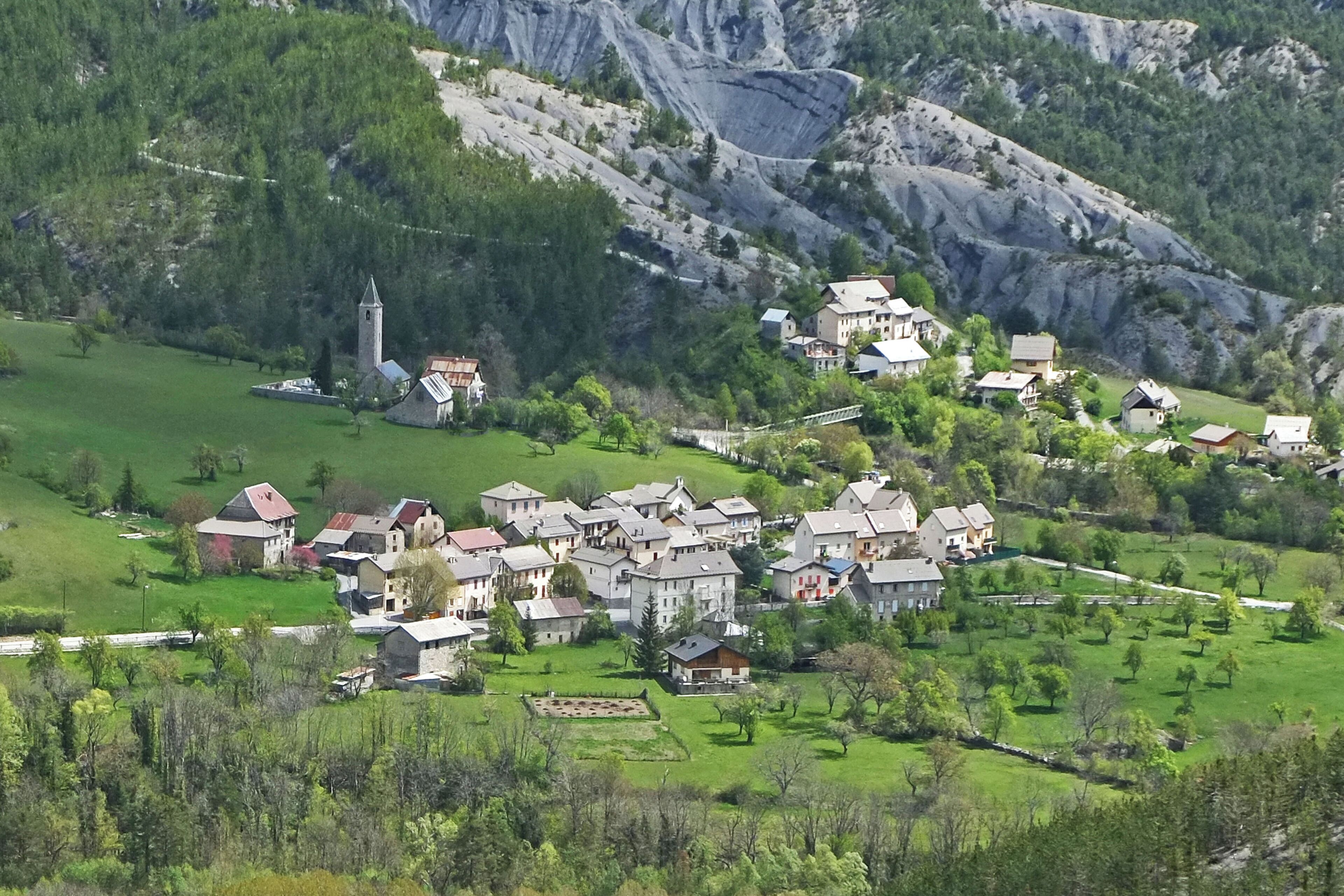 A village nestled in a valley with houses, a church, and a mountain backdrop.