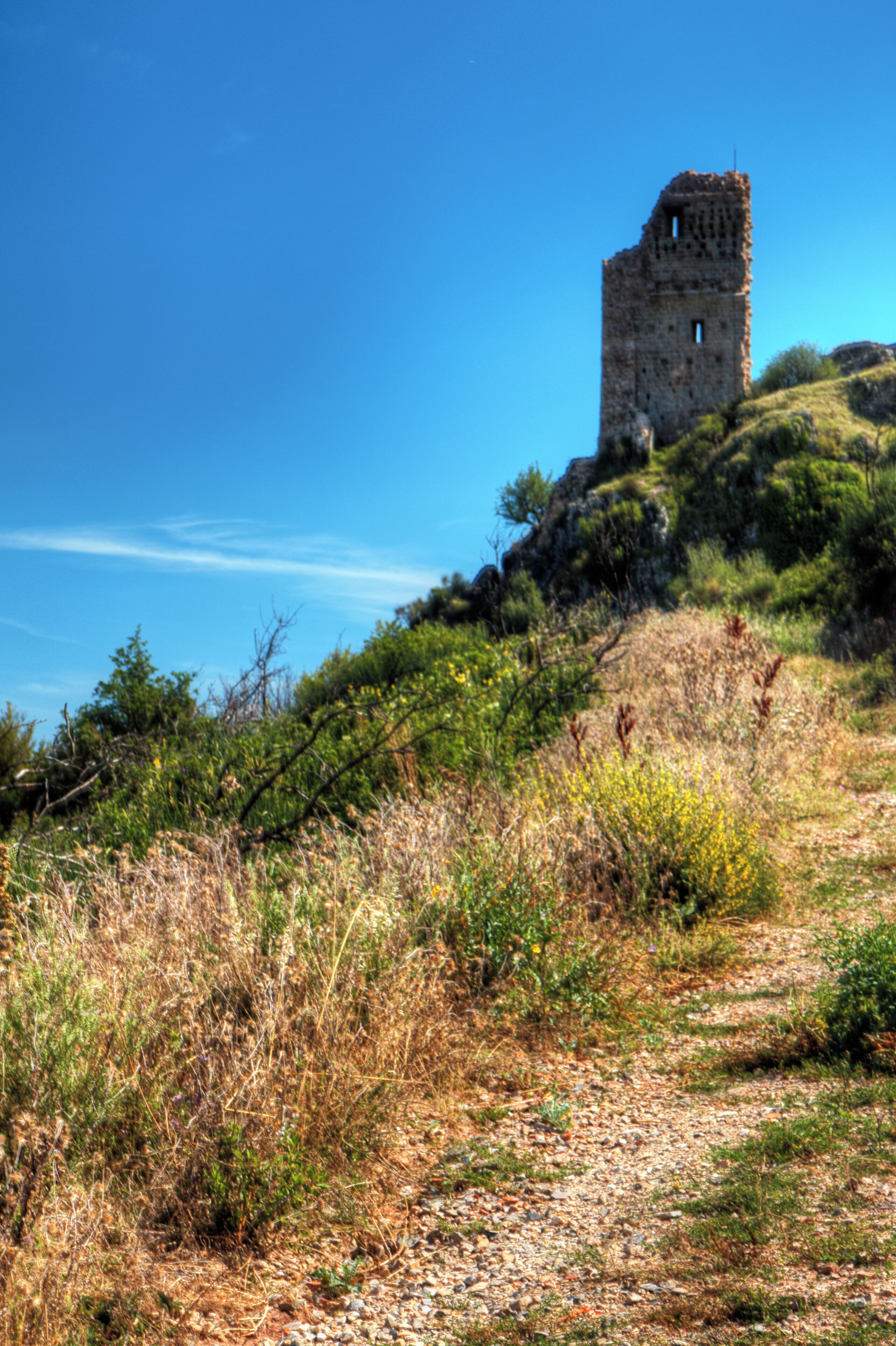 A stone tower on a grassy hill under a clear blue sky.