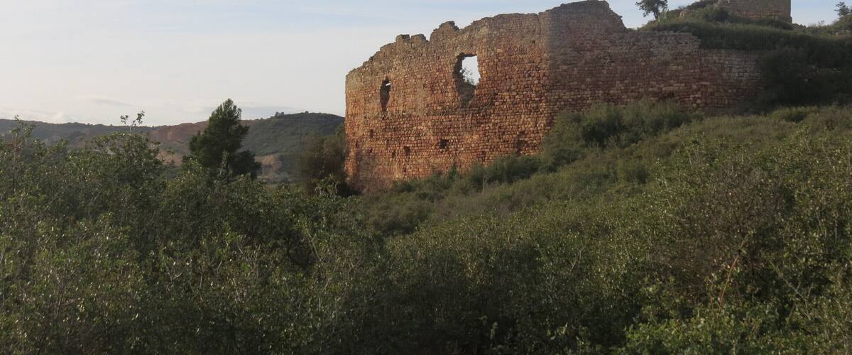 A ruined stone structure with a tall tower on a grassy hill.