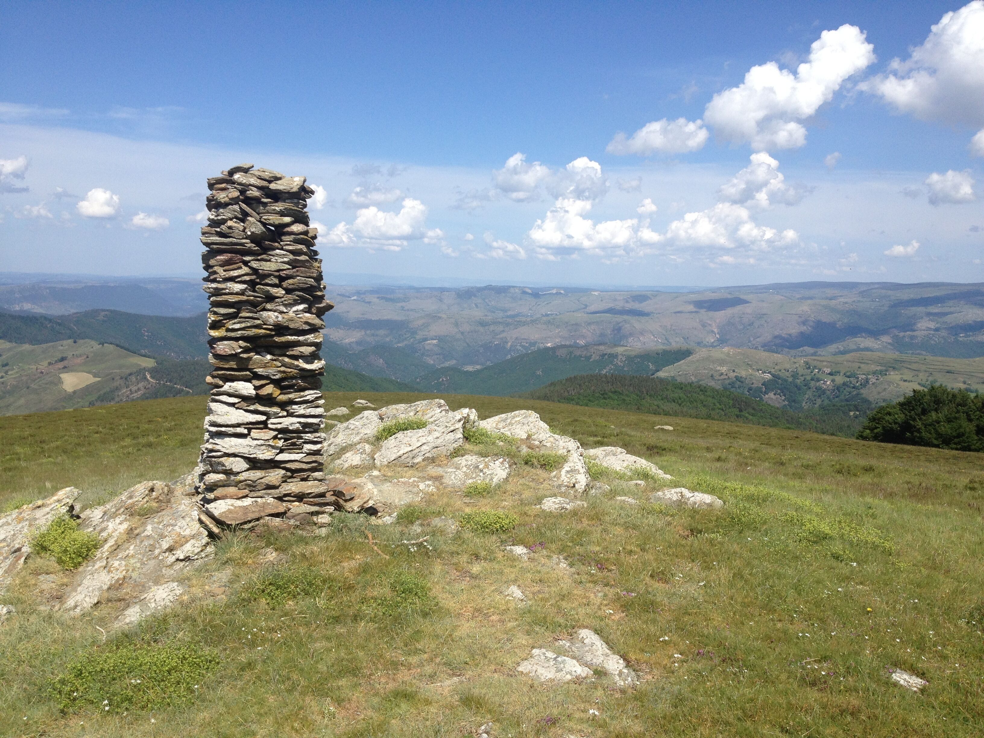 A stone pillar on a grassy hill with a panoramic view of rolling hills and valleys in the background.