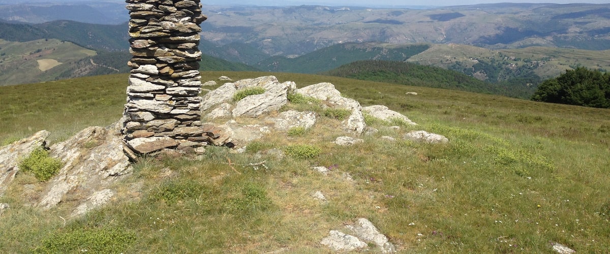 A stone pillar on a grassy hill with a panoramic view of rolling hills and valleys in the background.