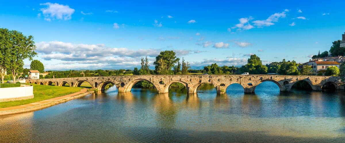 A stone bridge over a river, a castle on a hill, and lush greenery.