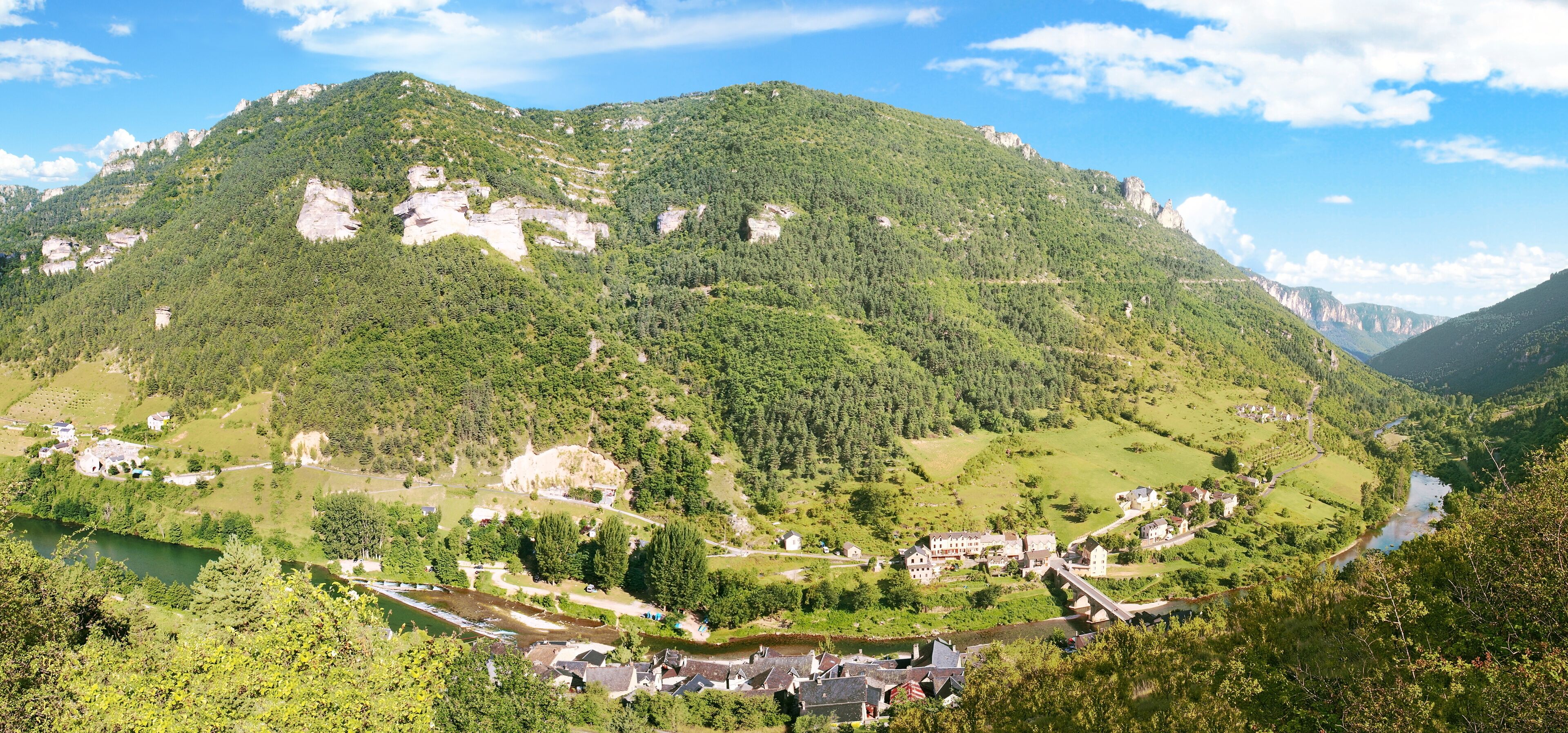 A mountainous landscape with a river, a small village, and a large rock formation.
