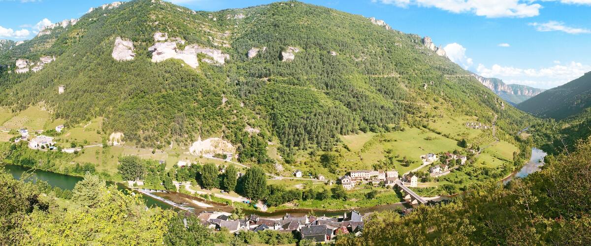 A mountainous landscape with a river, a small village, and a large rock formation.