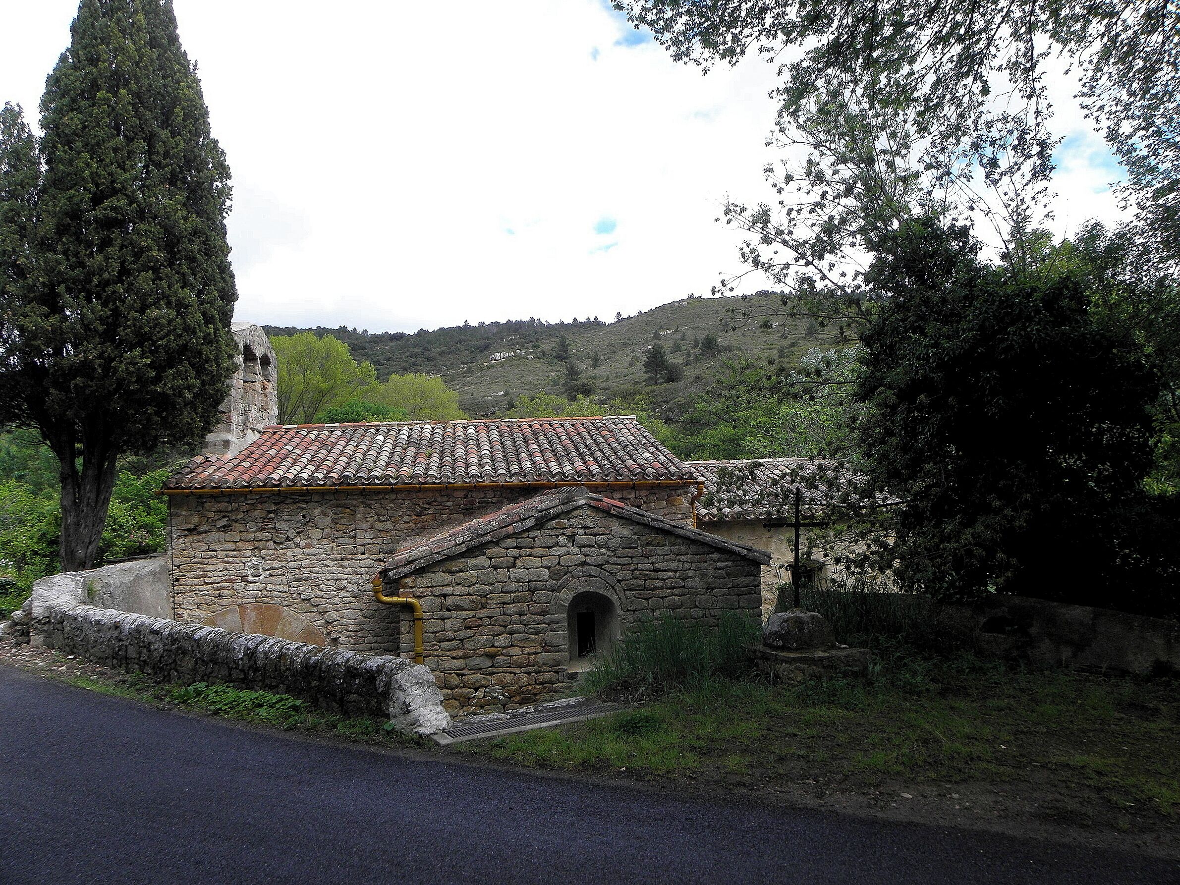 A stone building with a tiled roof, surrounded by trees and hills.