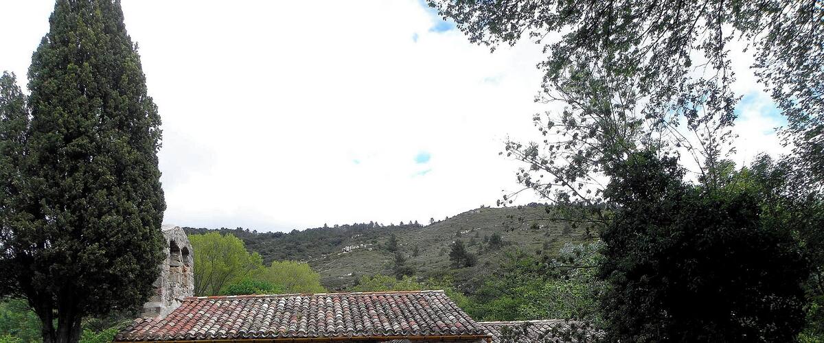 A stone building with a tiled roof, surrounded by trees and hills.