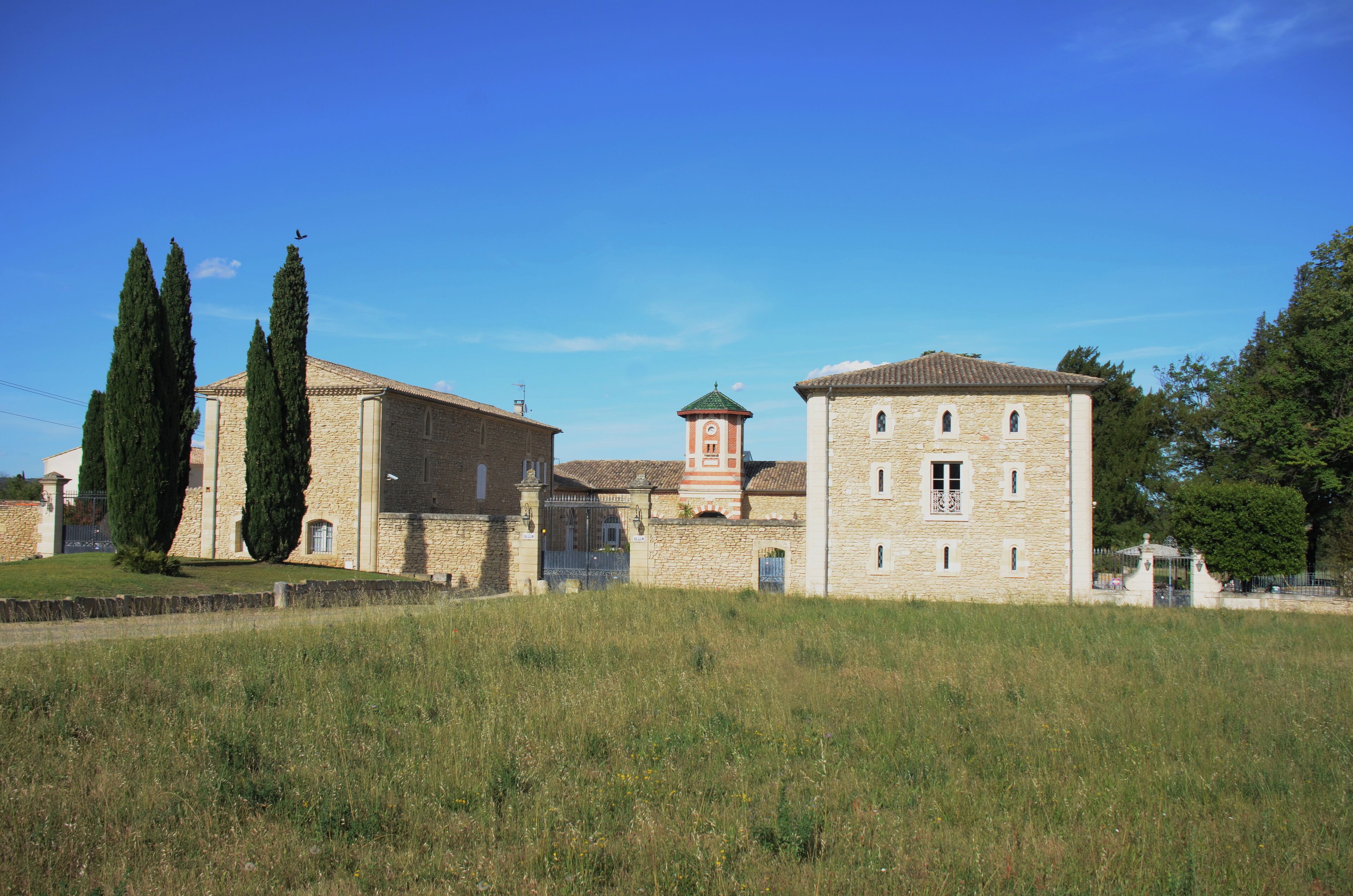 A stone building with a tower, surrounded by tall cypress trees and a grassy field.