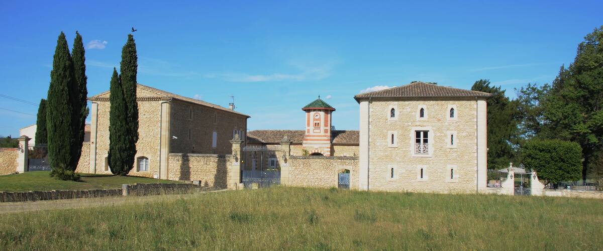 A stone building with a tower, surrounded by tall cypress trees and a grassy field.
