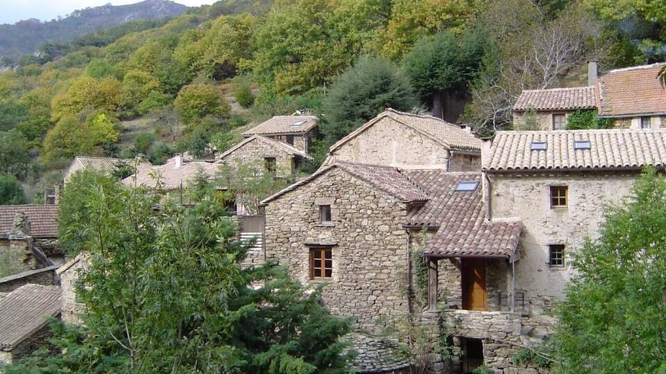 A village with stone houses, surrounded by lush greenery and hills.