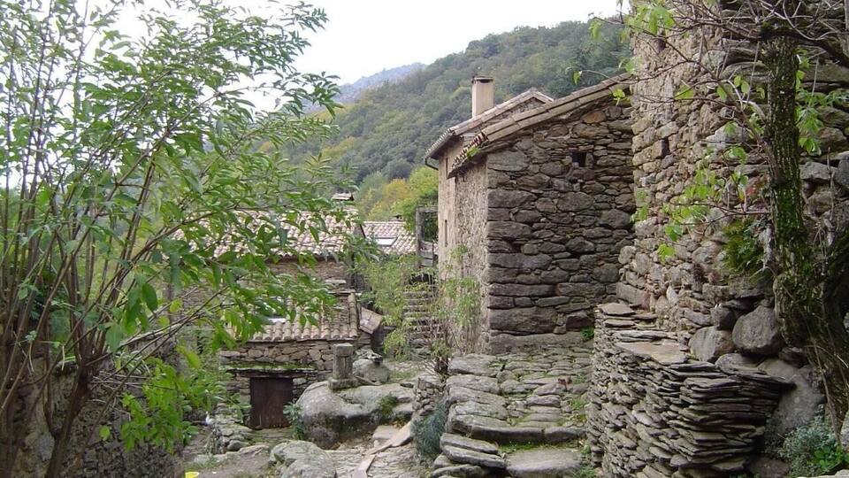 A stone building with a tiled roof surrounded by greenery and a stone wall.