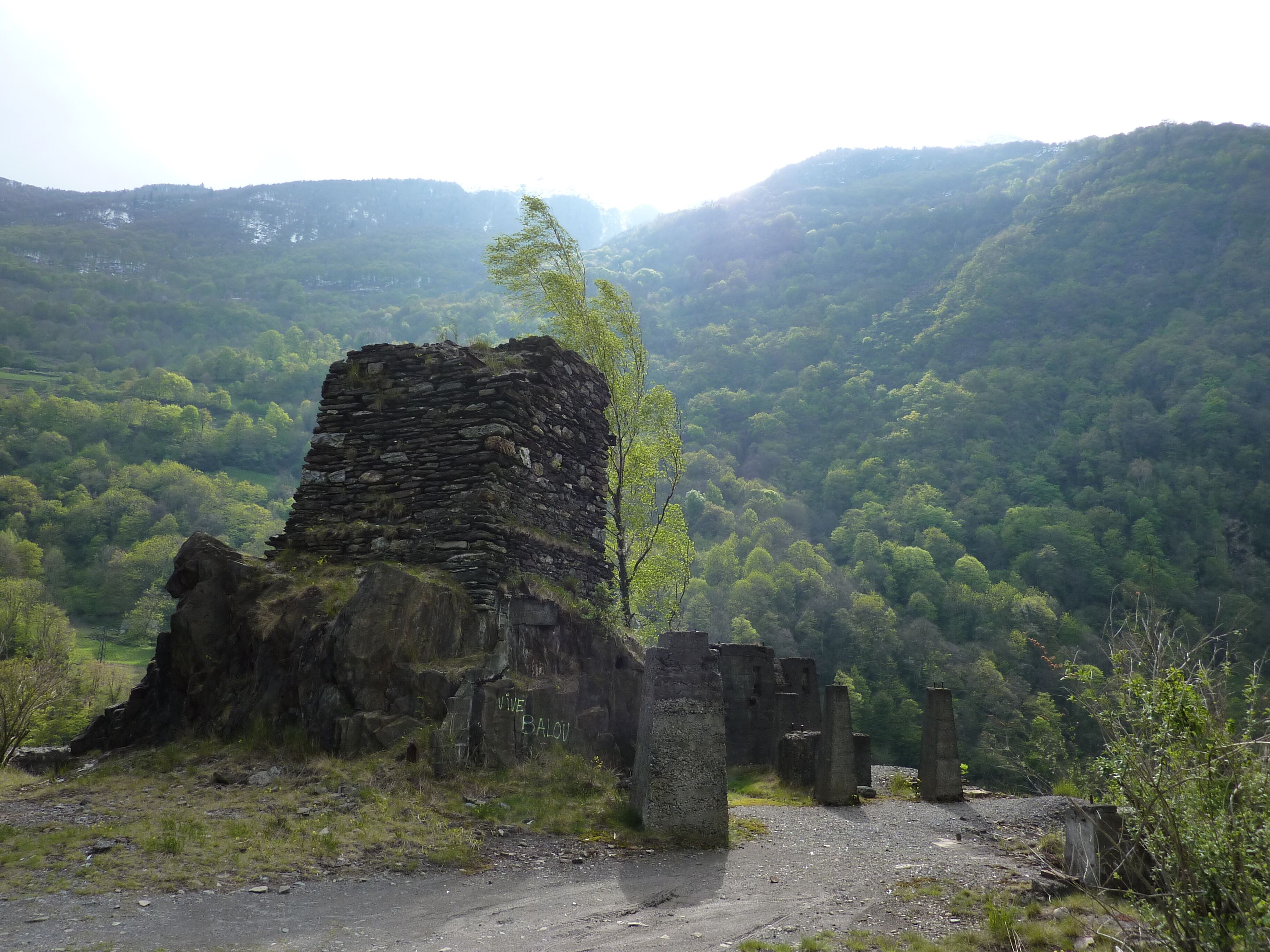 A stone ruin with inscriptions, surrounded by lush green hills and a clear sky.