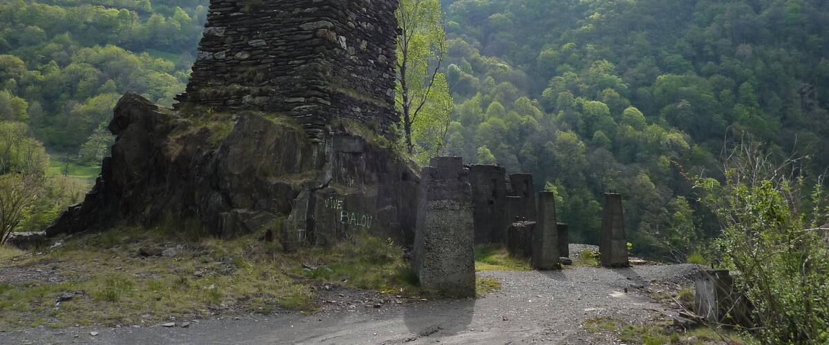 A stone ruin with inscriptions, surrounded by lush green hills and a clear sky.